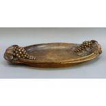 A large wooden oval bowl the sides deeply relief carved with grapes and vine leaves, 70cm wide