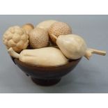 A studio pottery bowl of brown glaze containing a collection of hand carved wooden fruits