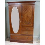 An Edwardian Sheraton Revival combination wardrobe with flared cornice, the left hand door with oval