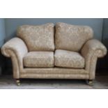 A two seater sofa upholstered in mustard coloured damask, squat square tapered legs with brass