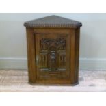 An oak corner cabinet having a single door carved with a figure within an arched niche and fluted