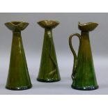 A set of three pottery ewers with uniform olive green glaze, the tricorn style spouts above wavy