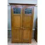 An oak Arts and Crafts wardrobe with flat cornice above a pair of door glazed to the top with