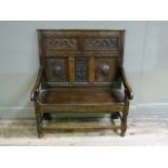 An oak hall settle in late 17th century style, the tall back carved with two foliate scroll panels