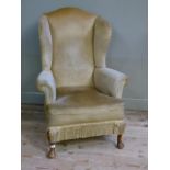 A 1920's mahogany winged armchair having an arched back, upholstered in pale gold Draylon with