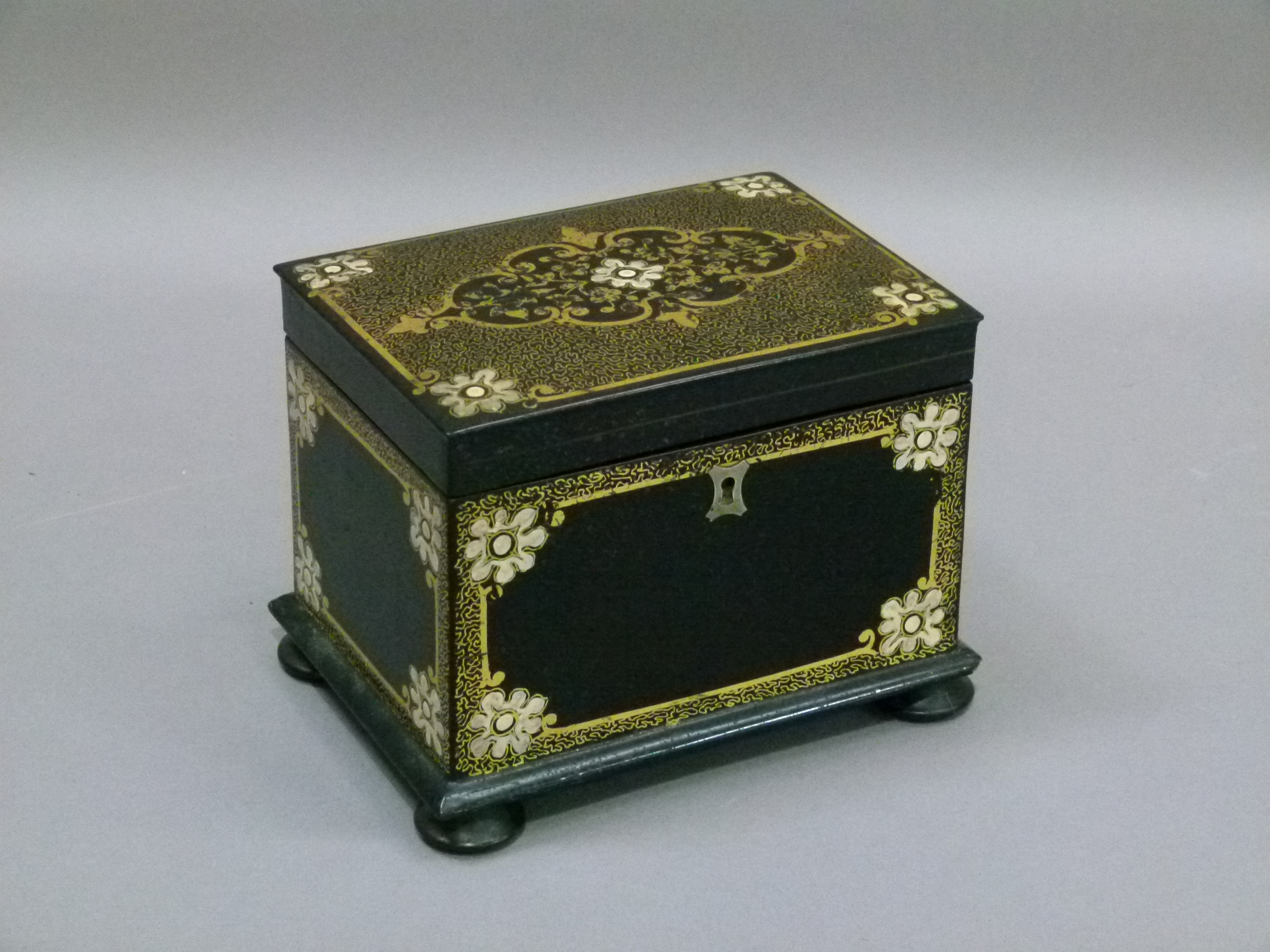 A Victorian black papier mâché tea caddy, the hinged lid with shaped floral filled cartouche on a