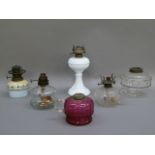 Six assorted oil lamps including a cranberry glass lamp base with clear glass handle