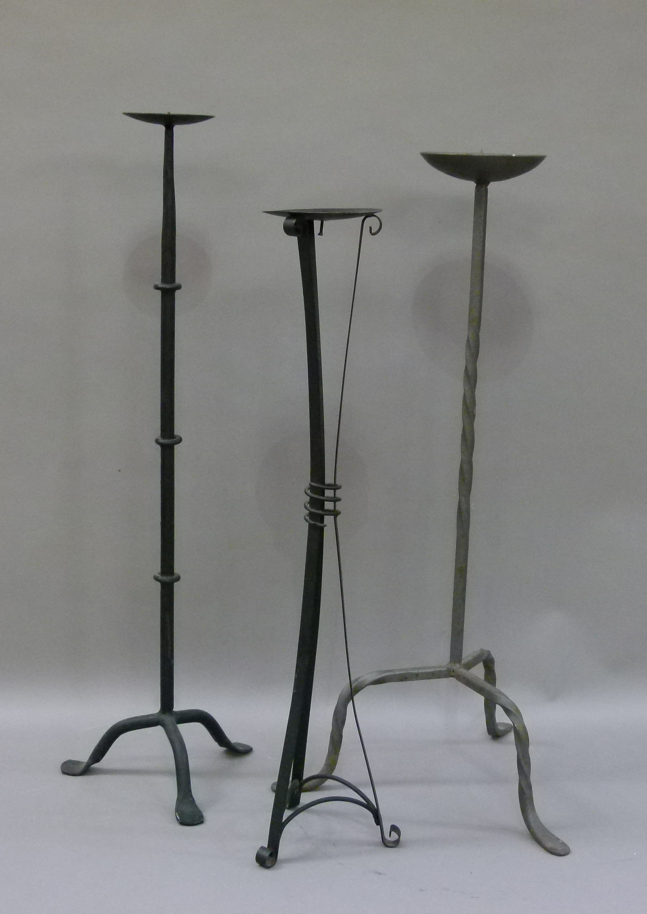 Two wrought iron candle stands and another three legged candle stand, 73cm high and smaller