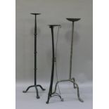 Two wrought iron candle stands and another three legged candle stand, 73cm high and smaller