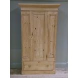 A pine wardrobe with flared cornice, central panelled door flanked by a pair of panels, long