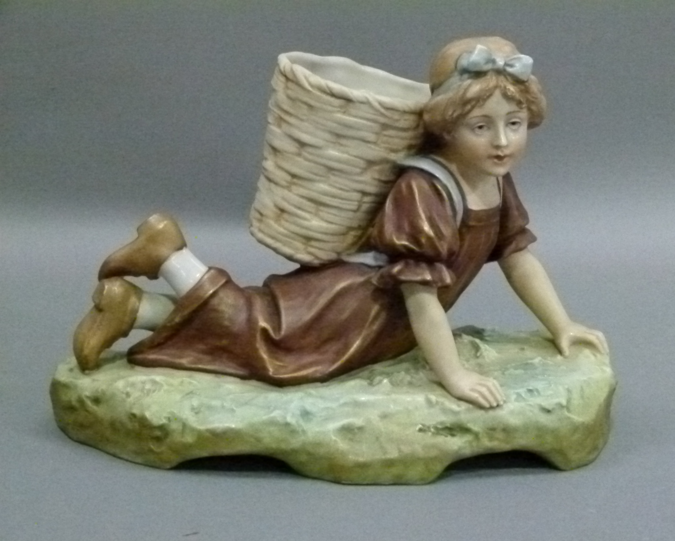 A Royal Dux porcelain figure of a young girl lying on her front with basket on her back, her hair in