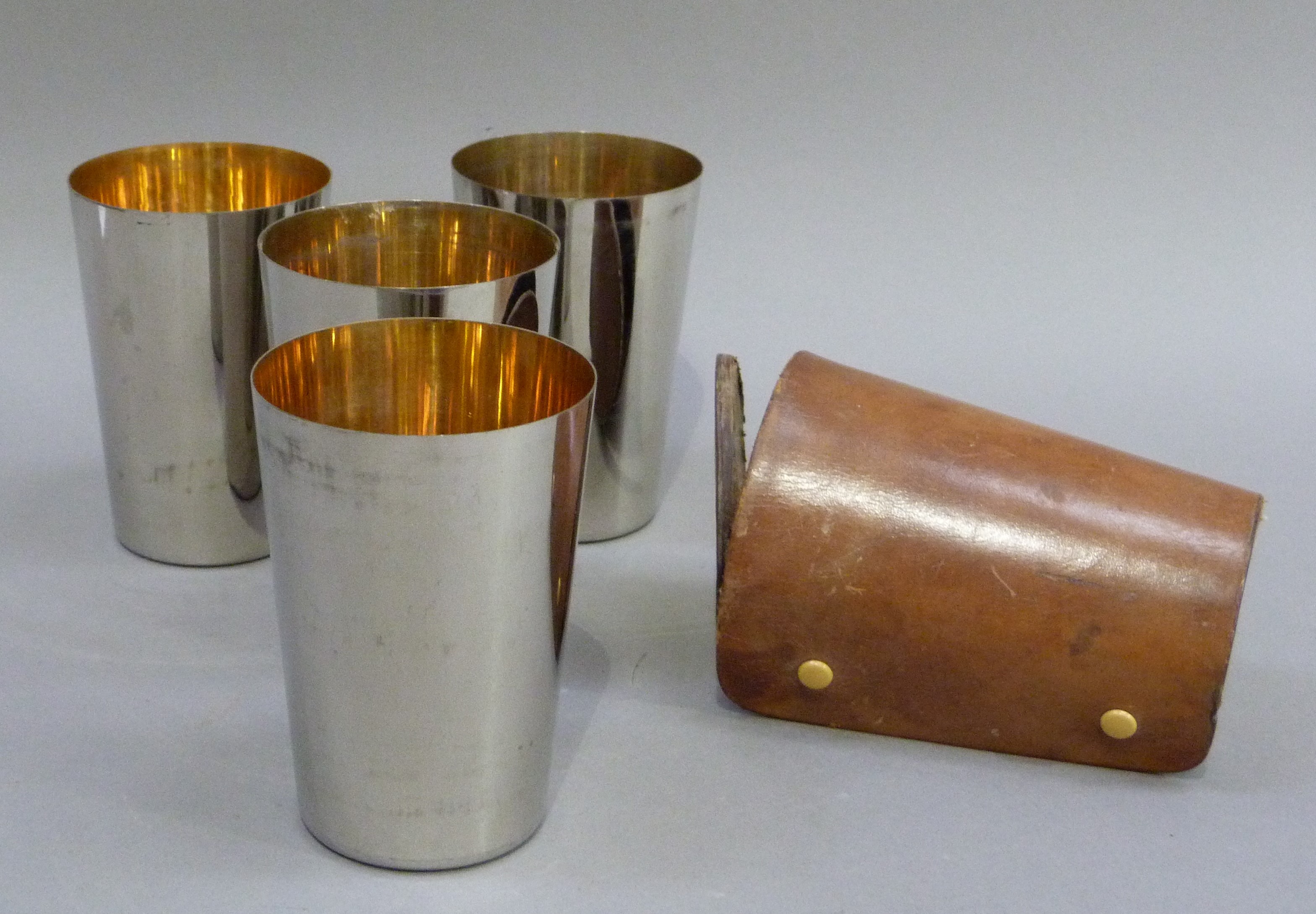 A set of four silver plated tumblers with silver gilt interiors in a leather carrying case