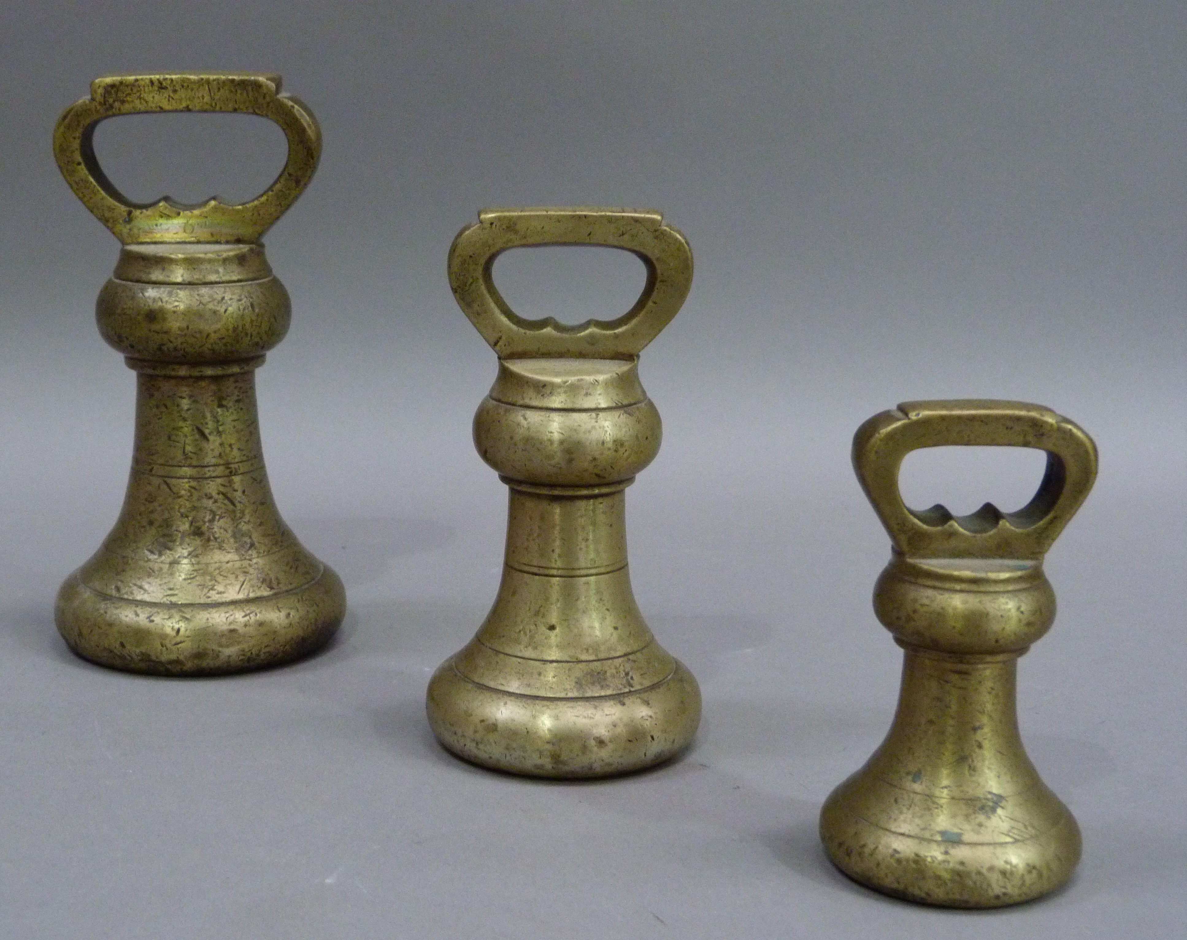 A graduated set of brass bell-shaped weights, comprising 7lbs, 4lbs and 2lbs, 7lbs weight 19cm