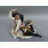 A Capo di Monte porcelain figure of a drunken cavalier resting on a rustic rococo plinth his right