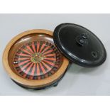 A circular wooden lidded roulette wheel with black and red printed board on ebonised base and bun