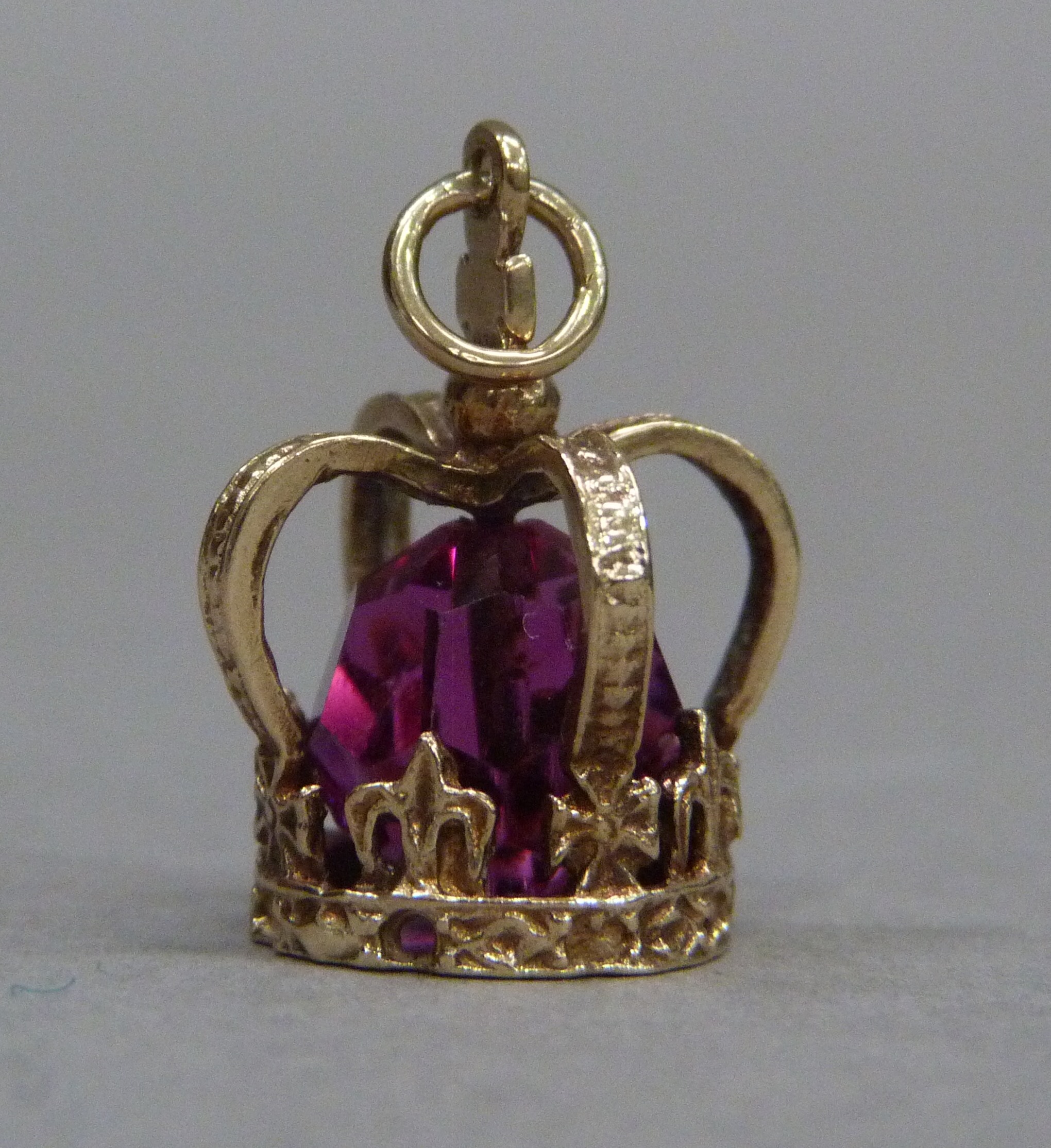 A crown charm in 9ct gold, c.1947, set to the centre with a faceted red paste bead, approximate