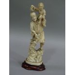 A carved ivory figure of a man with child on his shoulders, a rabbit at his right side, rustic base,