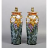 A pair of Doulton table lamps of slightly tapered cylindrical form decorated with vine leaves,
