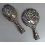 A silver mounted mirror and brush each embossed with flowers and leafage around a vacant shield-