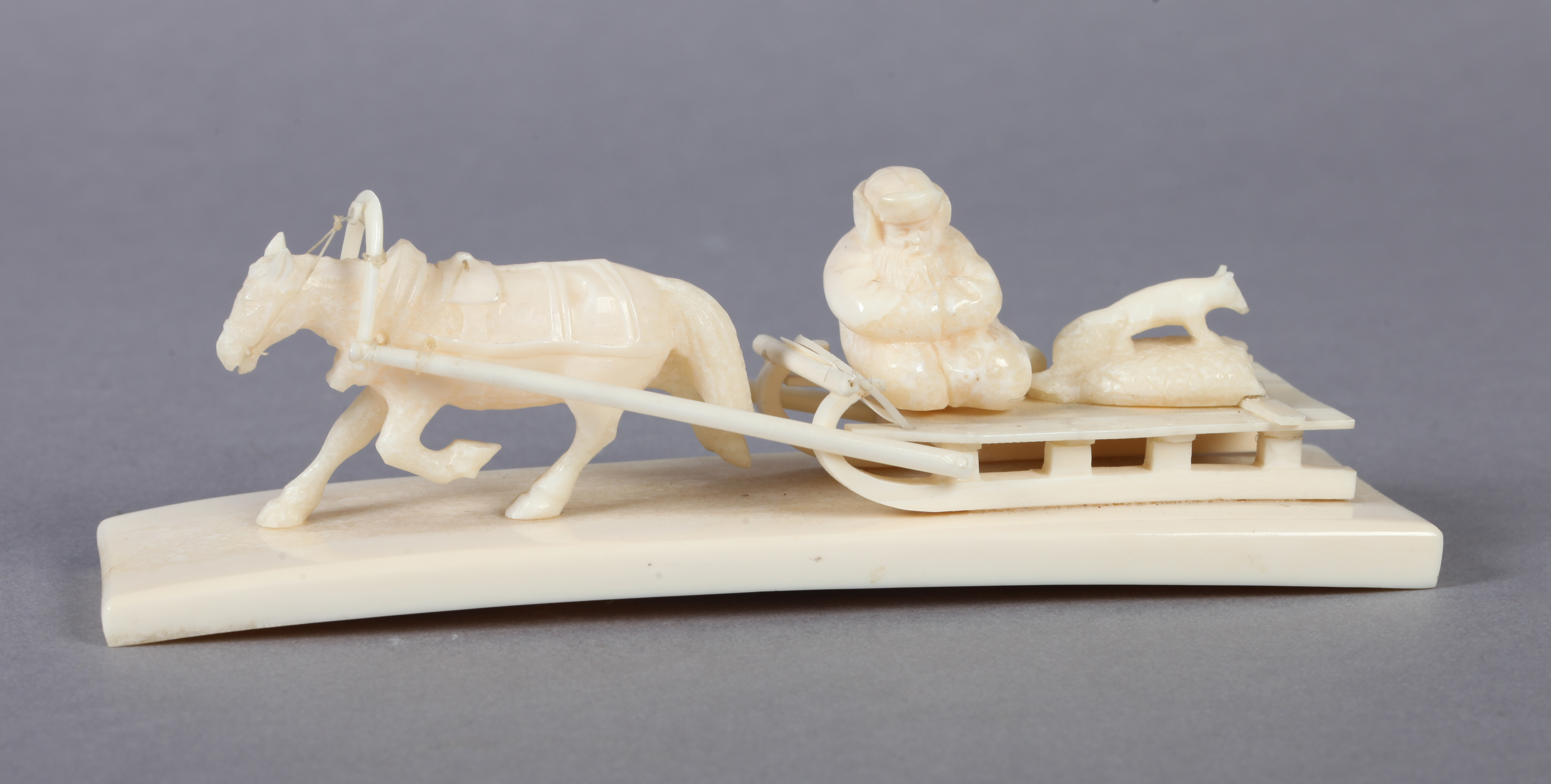 A WALRUS TUSK CARVING OF A HORSE pulling a low sledge, figure and fox on deck, tapered tusk fragment