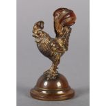 A MINIATURE GILT METAL CAST of a cockerel standing on a domed circular base, it holds a cornelian