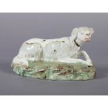 A VICTORIAN STAFFORDSHIRE POTTERY MODEL OF A RECUMBENT DOG on green/brown oval rustic base, 16cm