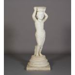 A WHITE MARBLE FIGURE OF A CHERUB, standing beside a bocage, holding a basket on his head, on a