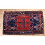 AN ANTIQUE PERSIAN HAND MADE NAHAVAND RUG, having a hooked triple panel medallion on an iron red