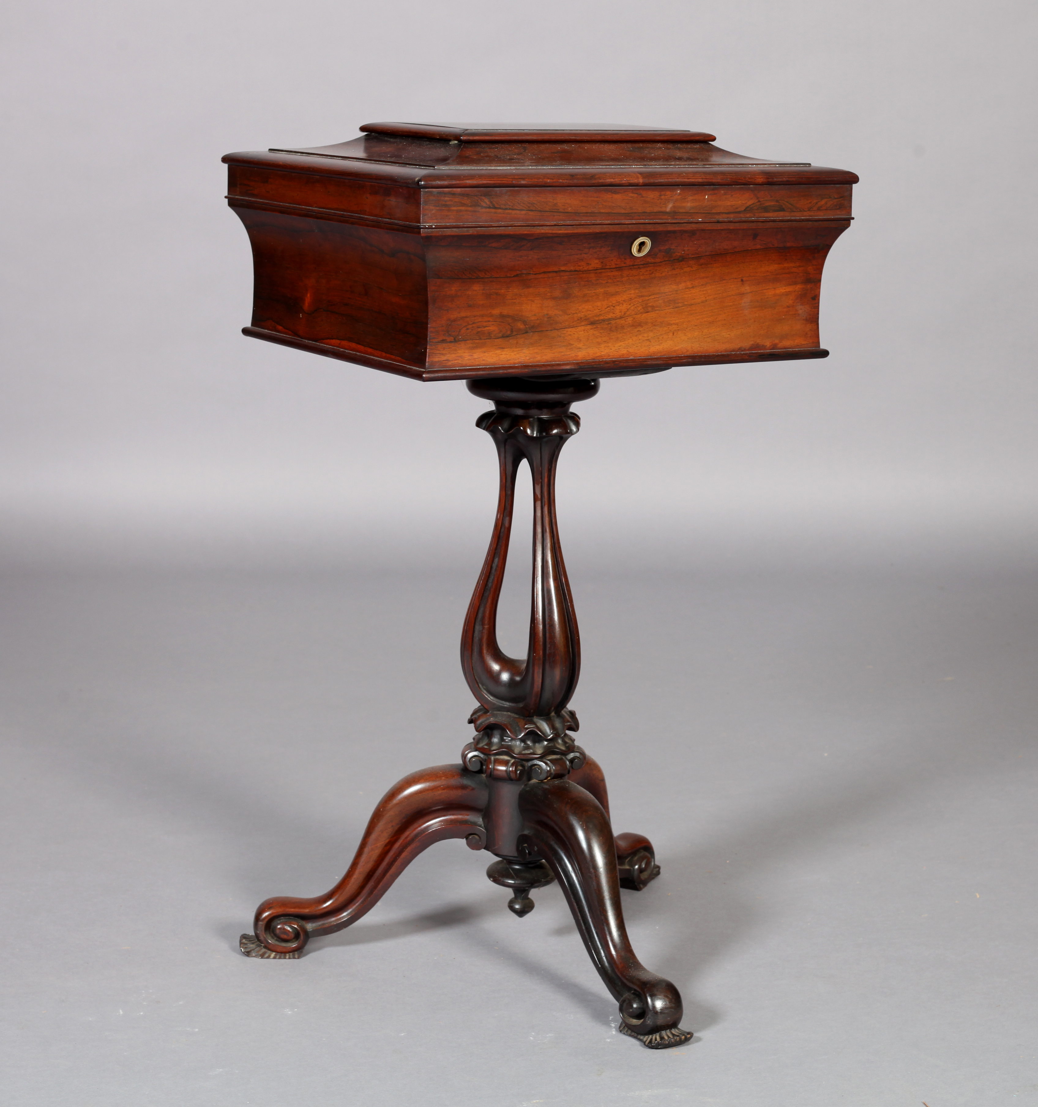 A VICTORIAN ROSEWOOD VENEERED TEAPOY, the shallow sarcophagus shaped top hinged to reveal an