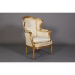 A LOUIS XVI STYLE GILTWOOD WINGED ARMCHAIR the encircling frame carved with pendants, musical trophy