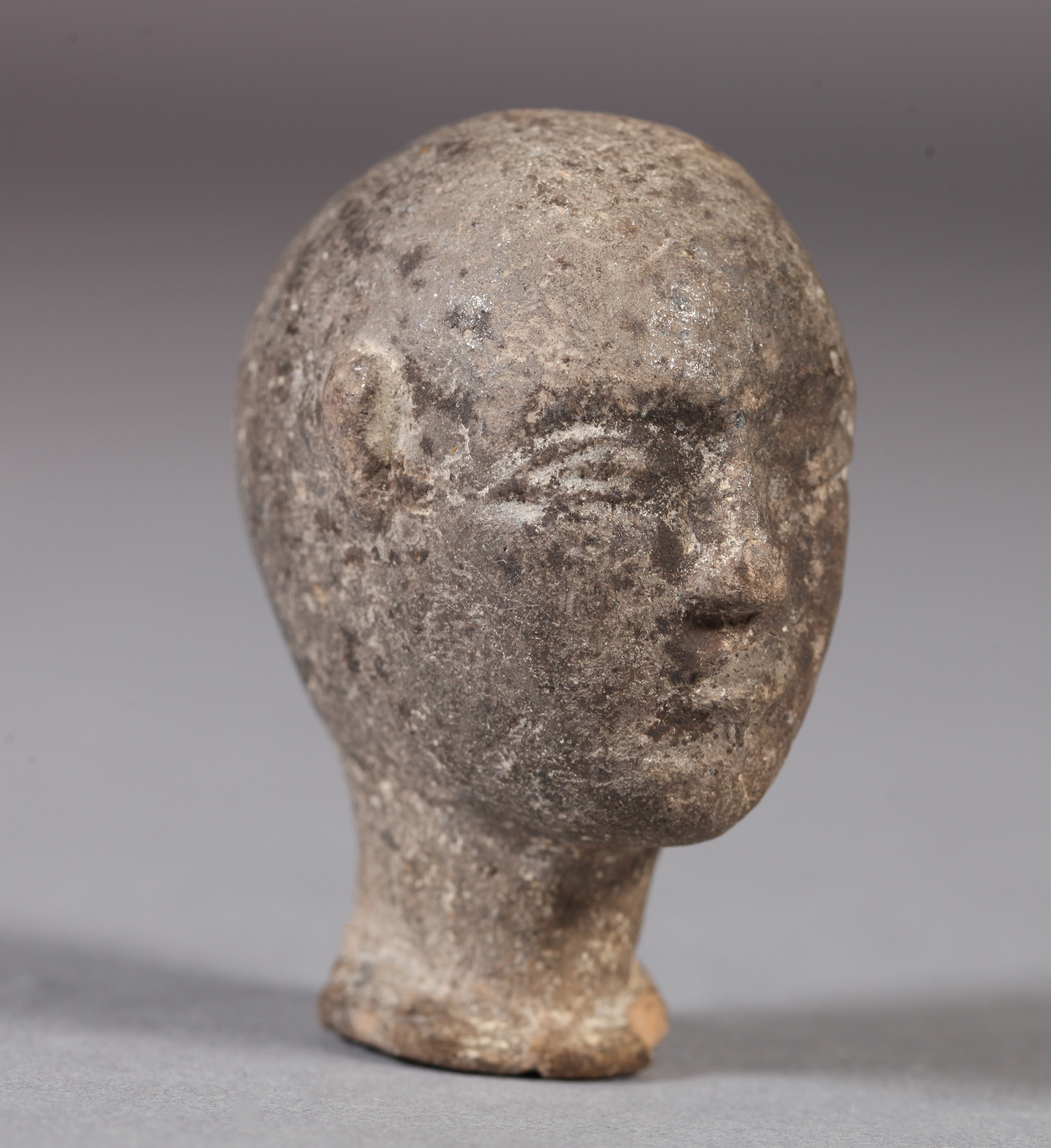 A SMALL POTTERY HEAD realistically modelled with bald pate, shallow oval neck, bearing traces of