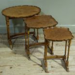 A nest of three shaped oval walnut veneered occasional tables with pie crust tops on ring turned
