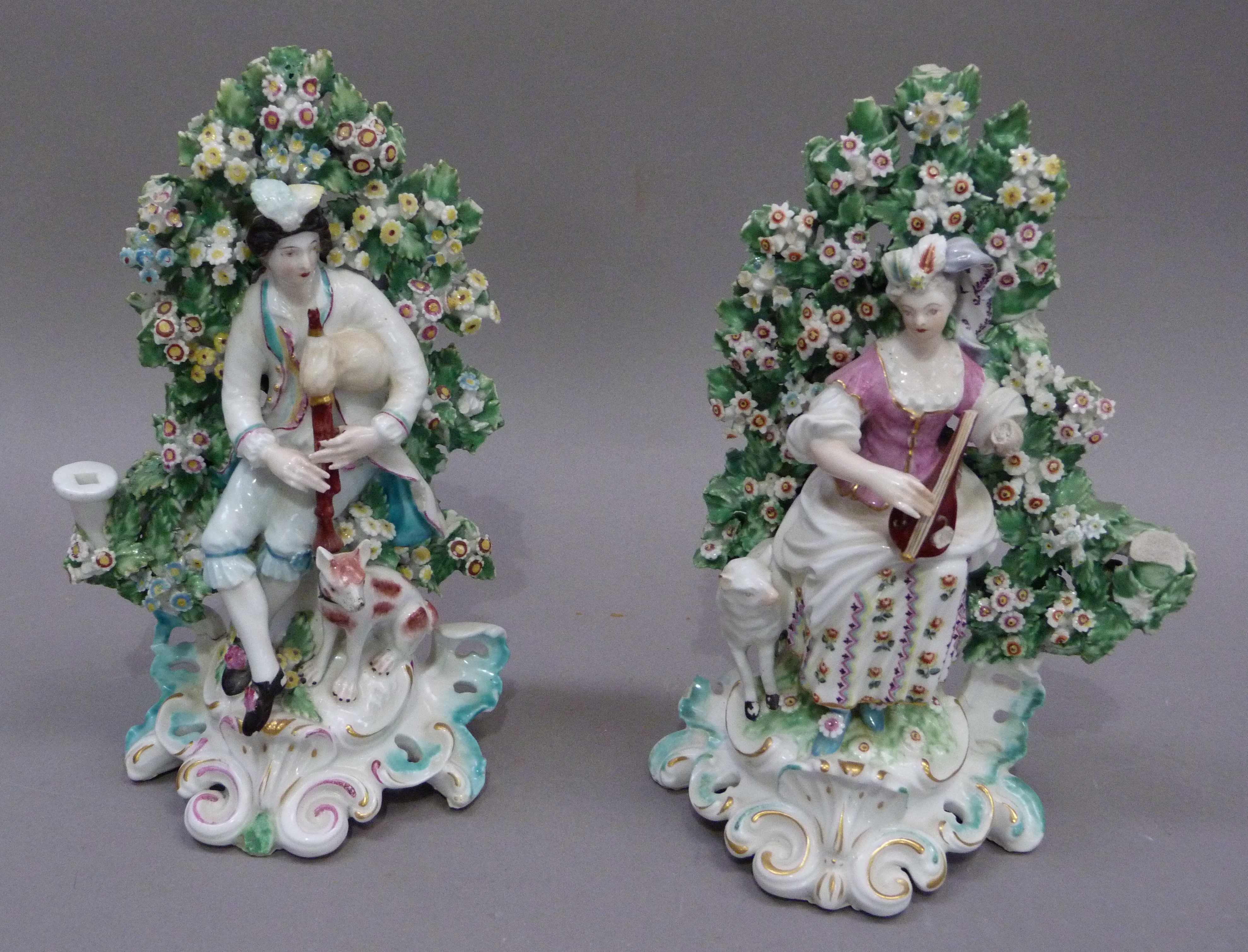 A pair of Derby porcelain seated bocage figures of a piper and hound and shepherdess with lamb,