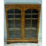 A reproduction burr walnut veneered display cabinet enclosed by a pair of glazed doors applied plain