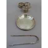 A silver circular dish, three silver napkin rings and a pair of Georgian sugar tongs with acorn