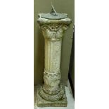 A concrete garden sundial with cast metal dial on a column, foliate cast to the top and with