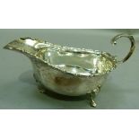 A silver sauce boat with bracketed rim and flying scroll handle on three hoof feet, Birmingham 1934,