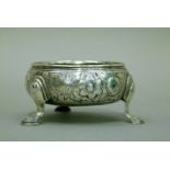 A mid 18th century silver open salt, circular, with embossed floral decoration on three hoof feet,