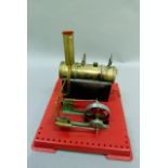 A Mamod stationary steam engine with 15.5cm boiler on a red metal base, 26cm square