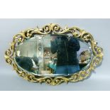 An oval bevelled wall mirror within a gilt scroll surround, approximately 76cm x 48cm