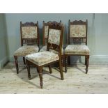 A set of four Edwardian oak framed dining chairs having a double arched top upholstered panel to the
