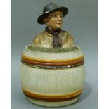 A 19th century Austrian pottery tobacco jar and cover modelled as a boy scout sitting in a barrel,
