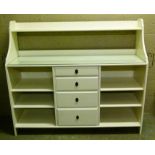 A shelf unit with swept back shelved above four central drawers flanked by open recesses with
