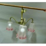 A brass electrolier having three scrolled arms with opaque and cranberry tinted glass shades with