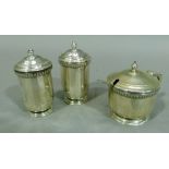 A three piece silver cruet of circular panelled form, comprising pepper, salt and mustard pot,