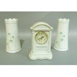 A Belleek mantel clock together with a pair of Belleek castellated topped tapered cylindrical