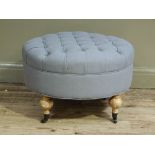 A modern upholstered circular stool with grey button fabric upholstery on four turned legs with