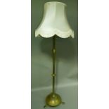 An Edwardian brass standard lamp on a circular base with three feet complete with shade