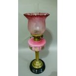 A Victorian brass and black glass oil lamp having floral painted pink reservoir and etched cranberry