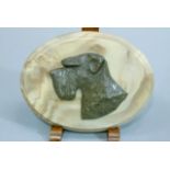A patinated metal relief bust of a terrier's head on an oval plaque, 18cm wide